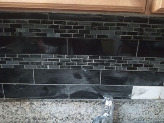 Real photo of a freshly installed dark glass tile kitchen backsplash by Morgan Carpet and Construction